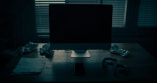 Dark home office with closed laptop, scattered papers, and handcuffs on wooden desk