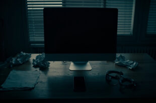 Dark home office with closed laptop, scattered papers, and handcuffs on wooden desk