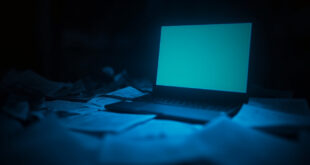Empty laptop screen glowing in dark room with legal documents scattered on desk surface