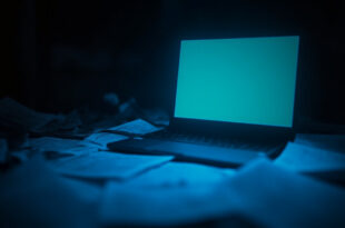 Empty laptop screen glowing in dark room with legal documents scattered on desk surface
