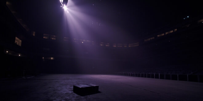 Empty concert stage with dramatic lighting in darkened stadium venue, abandoned briefcase visible on floor