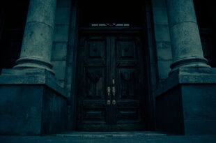 Classical government building entrance with heavy wooden doors and brass fixtures against overcast sky