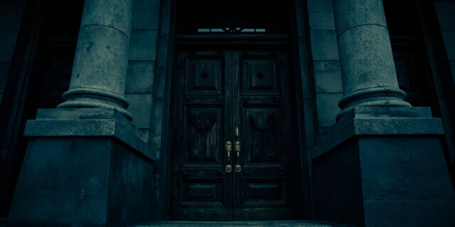 Classical government building entrance with heavy wooden doors and brass fixtures against overcast sky
