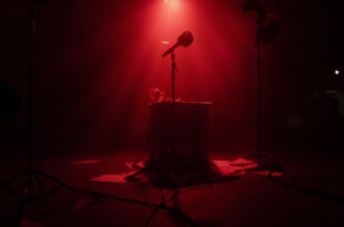 Empty television studio with host desk, microphone, and production lights in darkness representing broadcast suspension