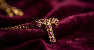 Gold chain necklace with ruby-adorned letter T pendant displayed against dark velvet surface