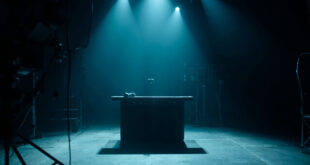 Empty television studio desk with microphone under spotlight, darkened screens and broadcasting equipment in background
