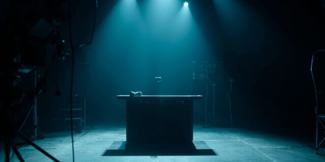Empty television studio desk with microphone under spotlight, darkened screens and broadcasting equipment in background