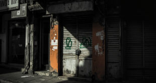 Closed storefront with padlock and medical prescription symbol, empty shelves visible through window
