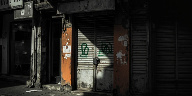 Closed storefront with padlock and medical prescription symbol, empty shelves visible through window