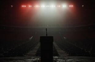 Empty stadium stage with lone microphone under bright spotlights, rows of vacant seats extending into darkness
