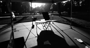 Empty folding table under white tent on campus with scattered papers and overturned chairs
