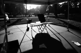 Empty folding table under white tent on campus with scattered papers and overturned chairs