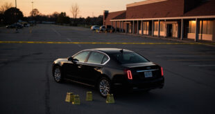 Empty parking lot with black car surrounded by police evidence markers and investigation tape at twilight