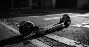 Black electric scooter lying on its side on concrete pavement near street intersection