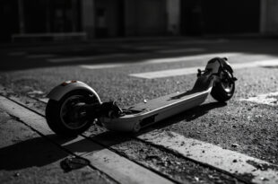 Black electric scooter lying on its side on concrete pavement near street intersection