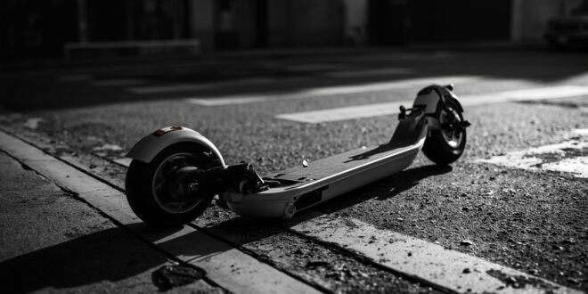 Black electric scooter lying on its side on concrete pavement near street intersection