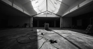 Empty white tent with scattered chairs and fallen microphone on university campus concrete