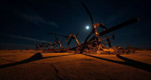 Destroyed helicopter wreckage with bent rotor blades on burned ground at night crash scene
