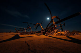 Destroyed helicopter wreckage with bent rotor blades on burned ground at night crash scene