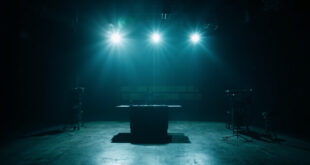 Empty television studio with single microphone under spotlight, vacant host desk, darkened stage and broadcasting equipment