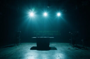 Empty television studio with single microphone under spotlight, vacant host desk, darkened stage and broadcasting equipment