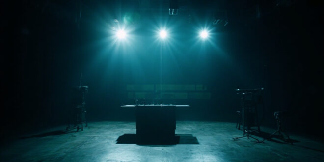 Empty television studio with single microphone under spotlight, vacant host desk, darkened stage and broadcasting equipment