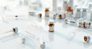 Empty vaccine vials and medical syringes arranged on white laboratory surface with prescription bottles