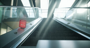 Static escalator in modern building lobby with red emergency stop button and safety equipment visible