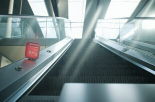 Static escalator in modern building lobby with red emergency stop button and safety equipment visible