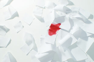Stacks of budget documents with red markings scattered across empty government office desk with calculators