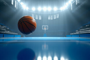 Orange basketball frozen mid-air approaching hoop in empty championship arena with dramatic overhead lighting