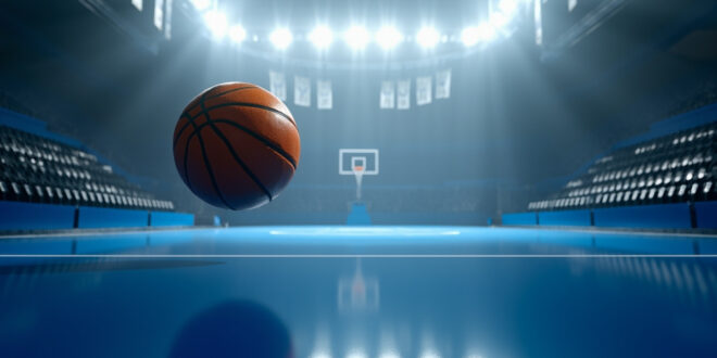 Orange basketball frozen mid-air approaching hoop in empty championship arena with dramatic overhead lighting