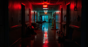 Empty institutional hallway with emergency lighting and medical equipment scattered on polished floor
