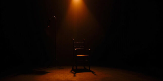 Empty black chair at podcast recording desk under focused studio lighting in darkened room