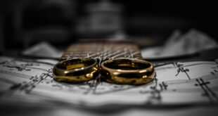 Two golden wedding rings rest on acoustic guitar strings in a modest apartment setting with medical recovery items nearby