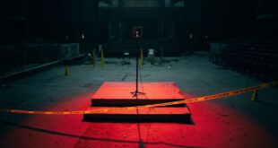 Empty podium with microphone on outdoor campus stage, yellow police tape visible, scattered folding chairs in background