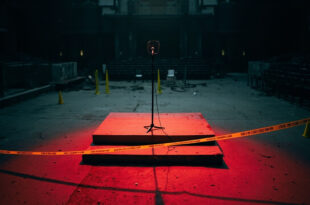 Empty podium with microphone on outdoor campus stage, yellow police tape visible, scattered folding chairs in background