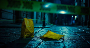 Yellow courier bag lies on cobblestone street surrounded by police tape and evidence markers in Lviv
