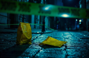 Yellow courier bag lies on cobblestone street surrounded by police tape and evidence markers in Lviv