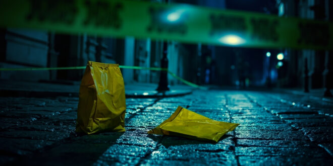 Yellow courier bag lies on cobblestone street surrounded by police tape and evidence markers in Lviv