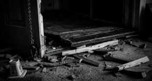 Broken wooden door with splintered frame and scattered debris on residential floor