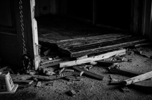 Broken wooden door with splintered frame and scattered debris on residential floor