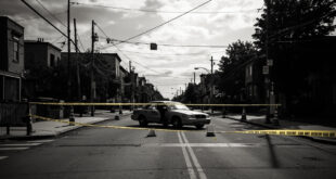 Empty urban street blocked by barriers, open car door, scattered traffic cones under overcast sky in residential area