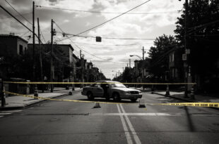 Empty urban street blocked by barriers, open car door, scattered traffic cones under overcast sky in residential area