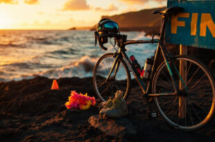 Triathlon gear and bicycle at Hawaiian coastal finish line with ocean and volcanic rock landscape at sunset