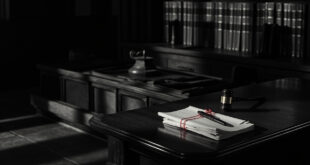 Closed legal files and gavel on dark wooden courtroom bench in somber lighting