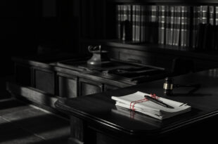 Closed legal files and gavel on dark wooden courtroom bench in somber lighting
