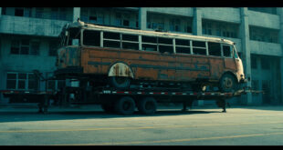 Weathered vintage bus secured on industrial flatbed trailer in depot yard