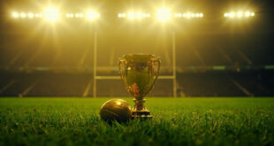 Championship rugby trophy stands illuminated on empty grass field under stadium floodlights
