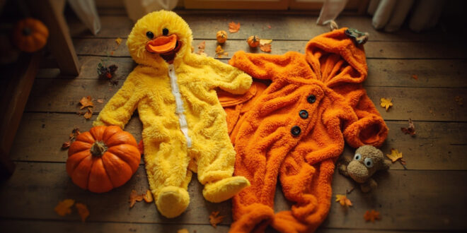 Yellow duck costume and orange pumpkin outfits with soccer ball on hardwood floor surrounded by autumn leaves